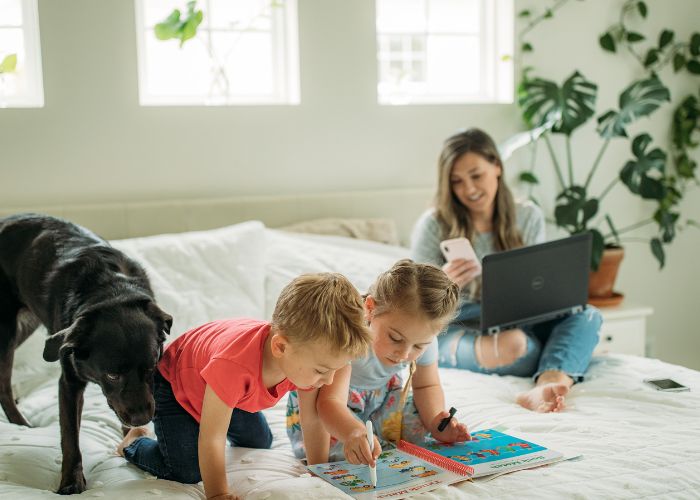 laptoppal és telefonnal dolgozó anya és két rajzoló kisgyermeke és fekete kutya