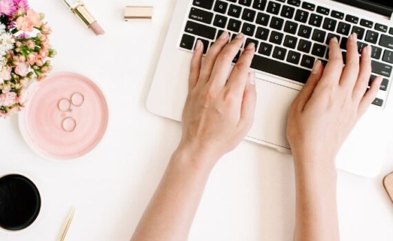 online adminisztrációt végző kezek laptop billentyűzeten íróasztalon és virág